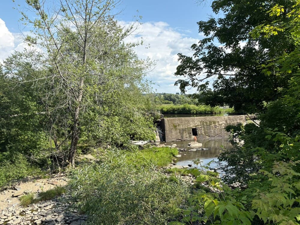 Ancien barrage de béton percé d'une ouverture, au-dessus d'un lit de rivière rocheux