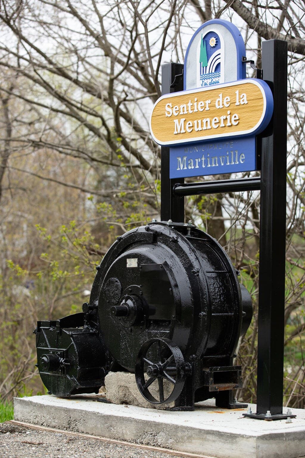 Le panneau du Sentier de la Meunerie et la turbine exposée à son pied